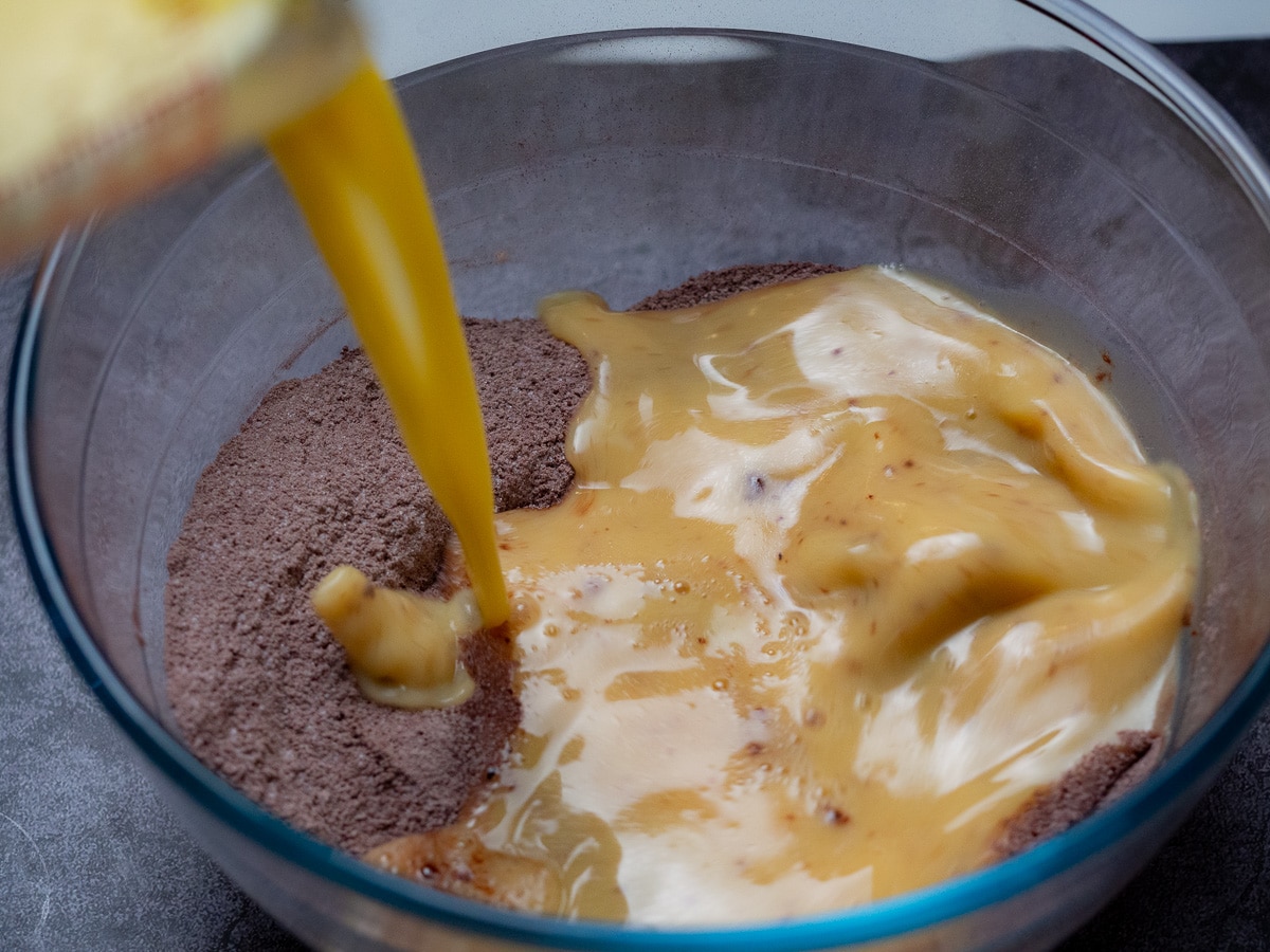 Adding butter mixture in the dry cocoa mixture in a large glass mixing bowl