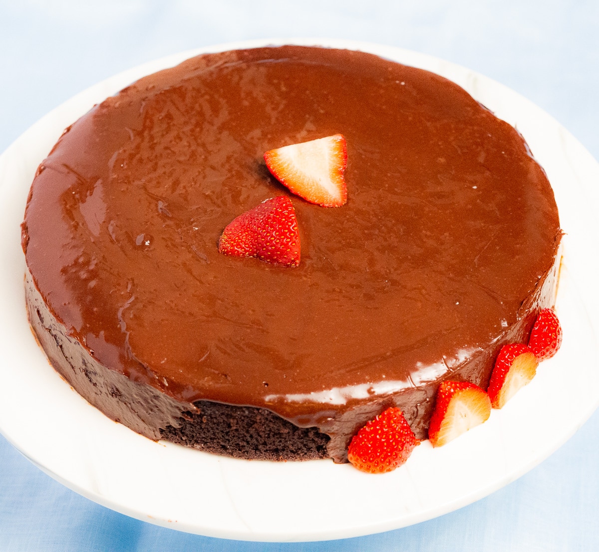 Chocolate fudge cake on a white cake stand  adorn with slices of strawberries.