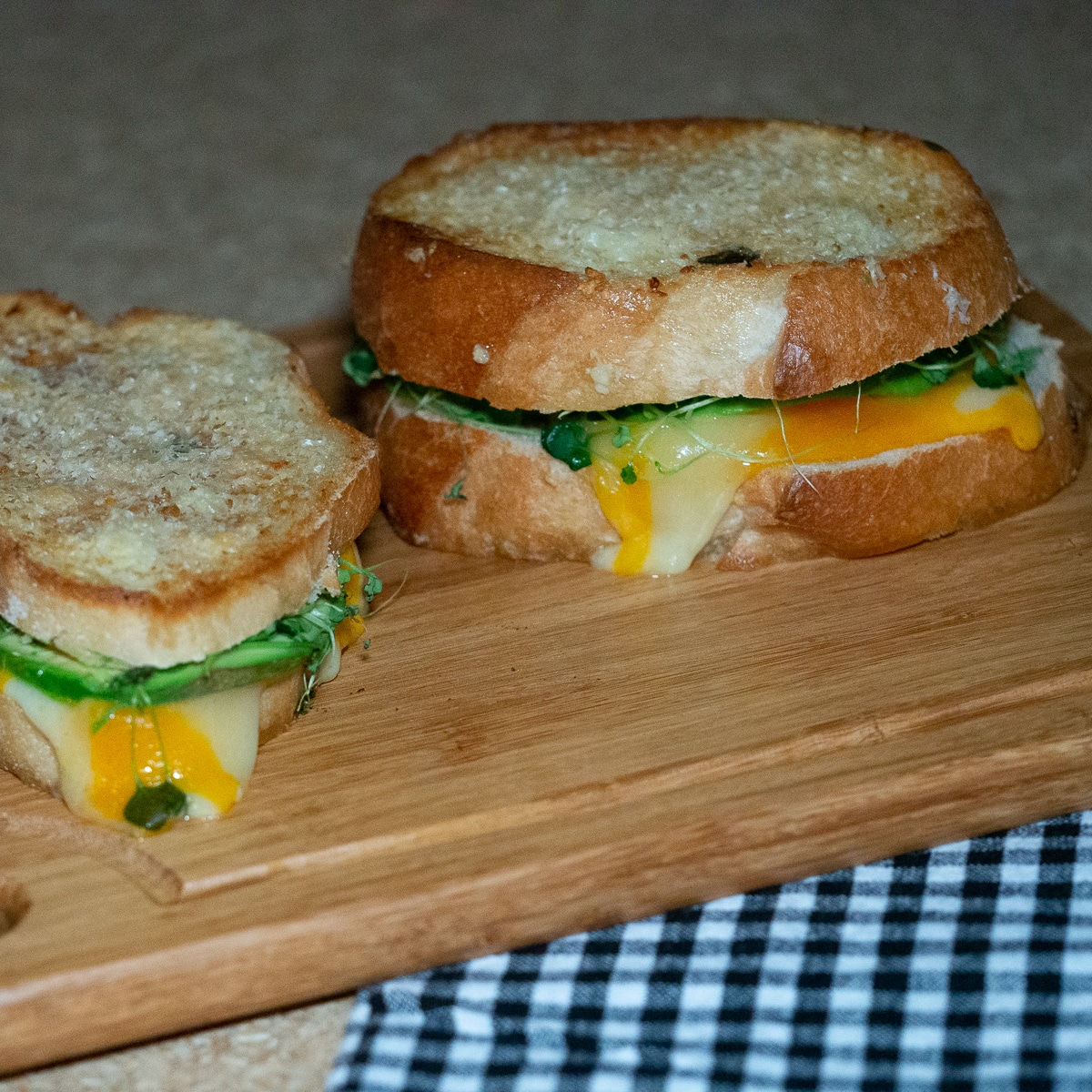 Grilled cheese sandwich filled with oozing cheese and avocado placed on top of wooden boardand