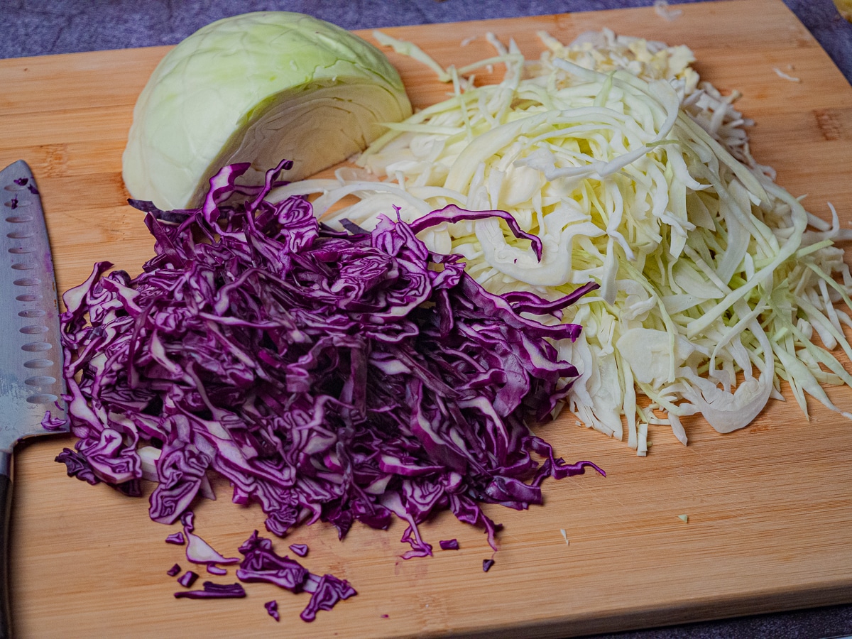 Thinly sliced green and purple cabbage placed on top of a chopping board.