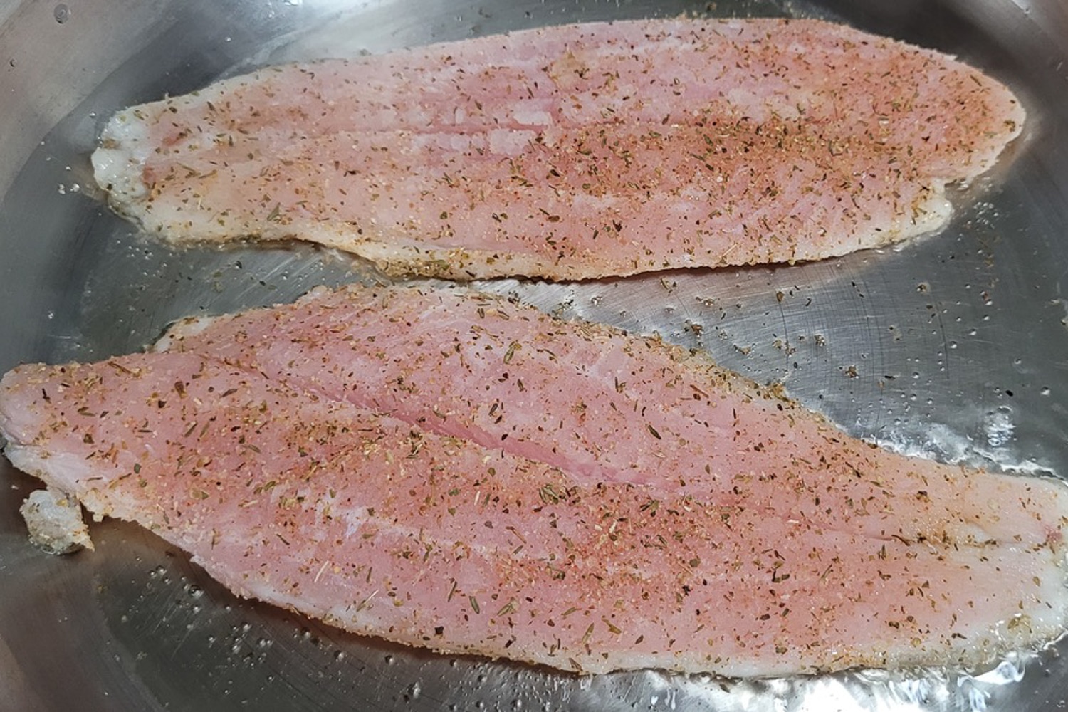 Saba fish fillet coated with italian seasoning on a frying pan.