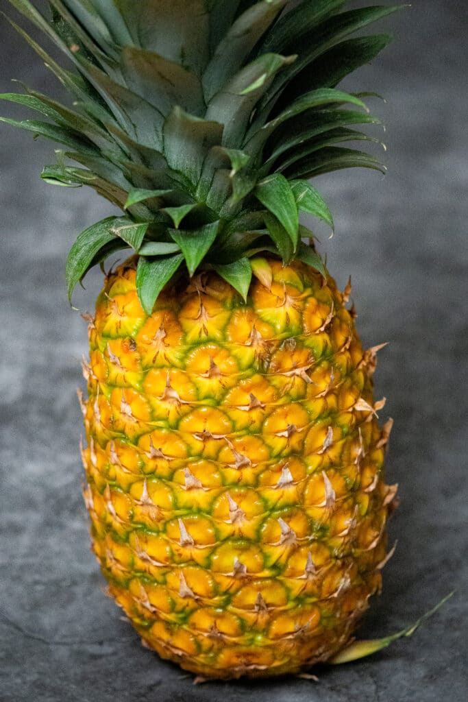 Golden yellow pineapple with its crown attached on a black and white countertop.